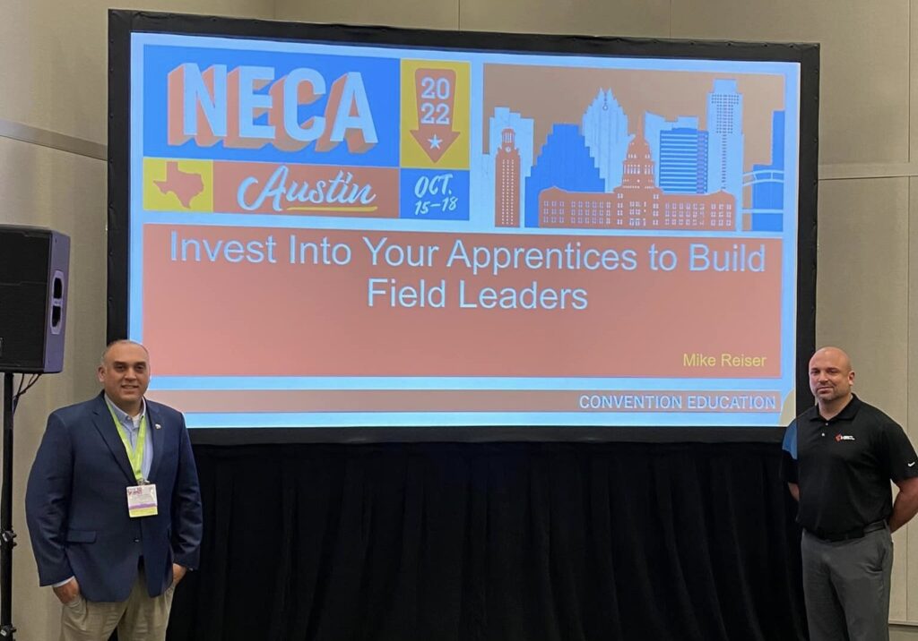 Bruno Frate and Michael Reiser pose in front of their presentation's title page at the 2022 NECA Convention in Austin, Texas.