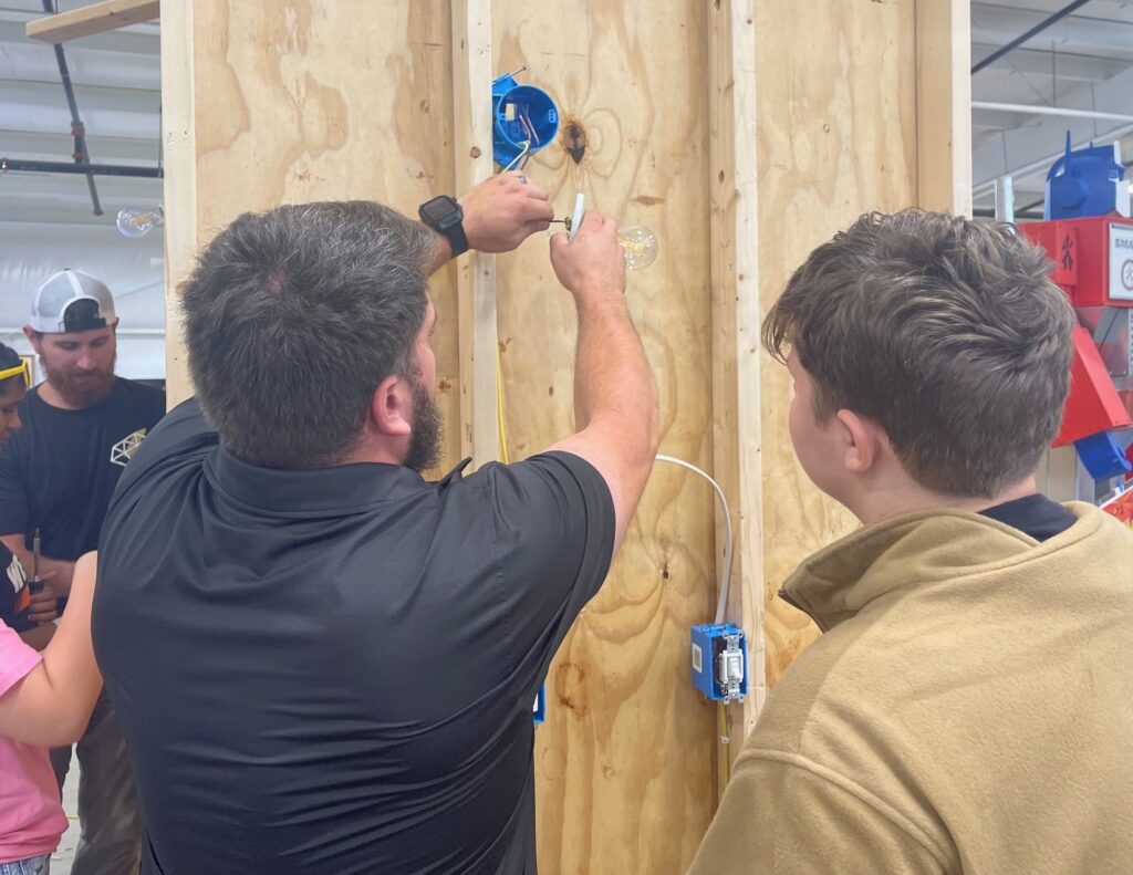 Middle school student learning about residential wiring from apprentice.